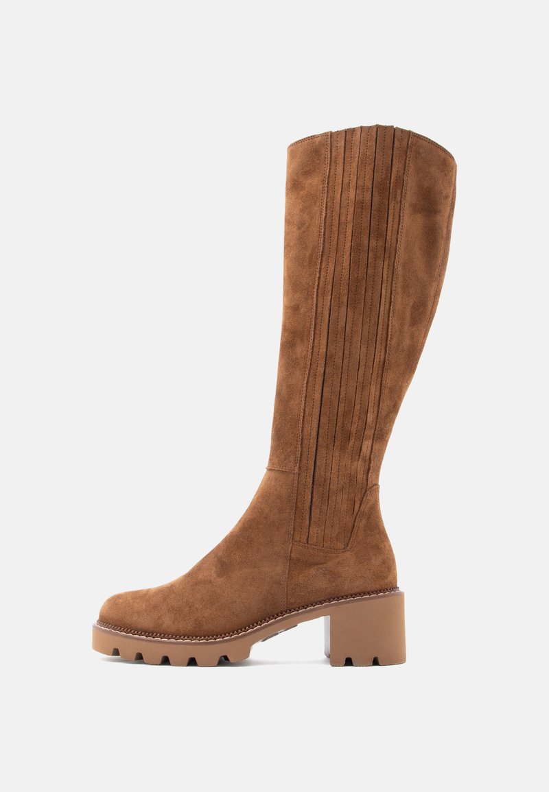 Vysoká hnědá suede bota s vyšitým vertikálním detailem, chunky podpatkem a objemnou podrážkou na jednobarevném světlém pozadí.