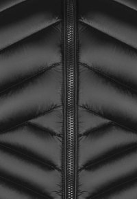 Svart puffer-väst med ett chevronmönster, glänsande yta och en central dragkedja. Tyget verkar slätt och vadderat.