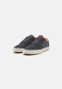 Navy blue canvas sneakers with orange accents, featuring round laces, rubber soles, and a smooth texture. Flat design with minimal branding.