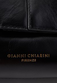 Produit en cuir noir avec un texte doré embossé indiquant "GIANNI CHIARINI FIRENZE." Texture lisse avec des détails de coutures visibles.