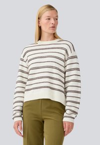 Maglione a righe bianco e marrone, con scollo rotondo, spalle cadenti e polsini e orlo a costine. Abbinato a pantaloni color oliva.