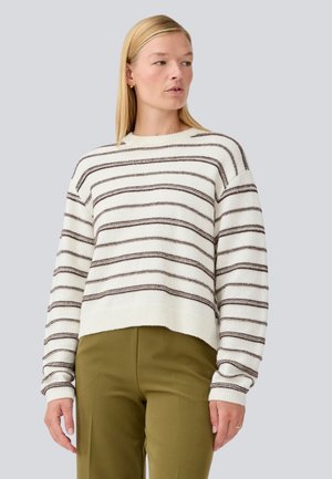 Maglione a righe bianco e marrone, con scollo rotondo, spalle cadenti e polsini e orlo a costine. Abbinato a pantaloni color oliva.