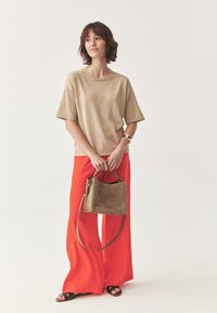 Top beige a maniche corte, pantaloni rossi a gamba larga e una morbida borsa marrone. L'outfit presenta una vestibilità rilassata e texture morbide.