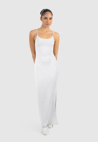 Vestido maxi blanco ajustado con tirantes finos y una tela suave y elástica. Presenta una silueta larga y recta con un diseño minimalista.
