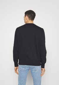Felpa nera con collo rotondo, spalle raglan e polsini a costine. Abbinata a jeans in denim azzurro chiaro, che mostrano un look casual.