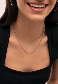 Collana in argento appoggiata su una clavicola nuda, con un design a maglie decorate, indossata sopra una maglia nera con scollatura quadrata.