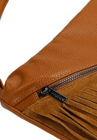 Braune Lederhandtasche mit strukturiertem Oberflächenmaterial, Reißverschluss und Wildleder-Fransen. Markenbeschläge sind am Reißverschluss sichtbar.