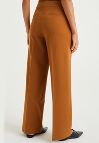 Vida byxor i orange-brun tyg med en mjuk textur, med hög midja, sidofickor och en enkel finish vid fållarna.