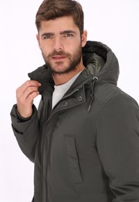Chaqueta verde oscuro con capucha, cierre delantero con cremallera y botones a presión. Cuenta con un bolsillo lateral y tela texturizada para mayor calidez y durabilidad.