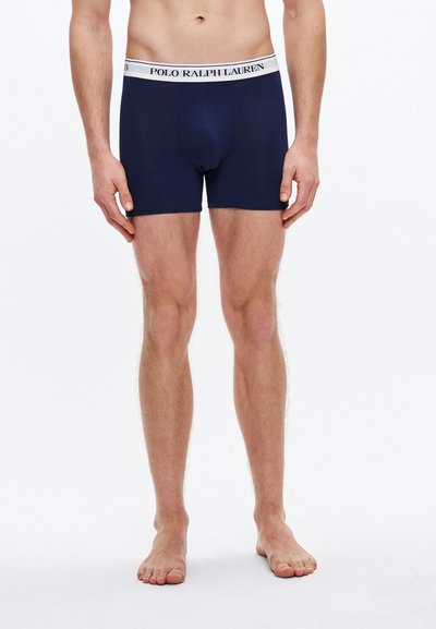Mornarsko modre bokserice iz mehke tkanine z belim pasom z napisom "POLO RALPH LAUREN", s prilegajočo se zasnovo in brez vidnih vzorcev.