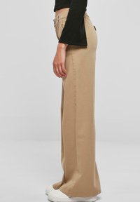 Beige wijdemouwen broek van katoen, met een hoge taille, zijzakken en een gladde textuur. Gepaard met witte sneakers.