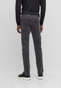 Vaqueros de mezclilla gris con un corte ajustado, con bolsillos traseros y detalles de costura evidentes. Combinados con zapatillas negras.