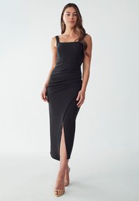 Black, form-fitting midi dress, featuring a square neckline, wide straps, and a side slit. Textured fabric and subtle shaping details.