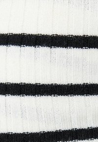 Tessuto a maglia con righe orizzontali alternate bianche e nere. La texture è a coste con cuciture visibili e un aspetto morbido e flessibile.