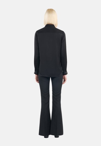 Blusa nera con colletto, maniche lunghe e polsini con bottoni. Abbinata a pantaloni neri a campana con un leggero motivo testurizzato.