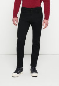 Μαύρο τζιν με λεπτή εφαρμογή, διαθέτει πέντε τσέπες, θηλιές για τη ζώνη και κανονικό κουμπί κλεισίματος. Φοριέται με γκρι sneakers ψηλής κορυφής.