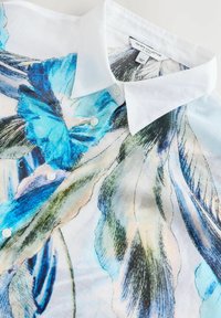 Korte mouwen shirt van lichtgewicht stof, met een blauw en groen bloemmotief, witte kraag en knoopsluiting.