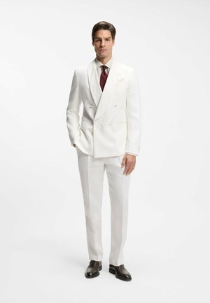 White double-breasted suit jacket, matching trousers, light striped shirt, and dark tie. Brown leather shoes add contrast.