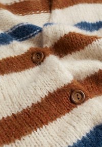 Zbliżenie na dzianinę w kolorach kremowym, rdzawego oraz niebieskiego w paski, z dwoma brązowymi guzikami przyszytymi do materiału.