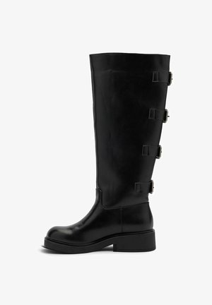 Botte noire en cuir montant jusqu'au genou avec quatre sangles à boucles latérales et un petit talon carré, vue de profil sur fond blanc.