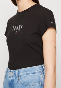 Zwarte katoenen t-shirt met korte mouwen, met het 'TOMMY JEANS' logo in het wit. Gepaard met lichtblauwe denim jeans.