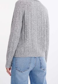 Szary sweter w splot kablowy o luźnym kroju, z prążkowanymi mankietami i krawędzią, zestawiony z jasnoniebieskimi, wysokim stanem dżinsami.
