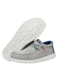 Scarpe slip-on grigio chiaro con superiore testurizzato, accenti blu e una suola maculata bianca. Presentano un design con lacci e un logo sulla linguetta.
