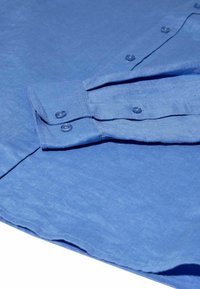 Ilga rankovė mėlyna marškiniai su sagomis, išdėstyti gulintys, rodant apykaklės manžetę su dviem sagomis ir dalį sagų juostos, ant balto fono.