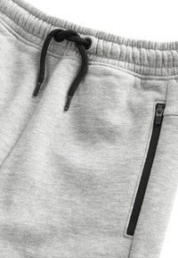Šedé tepláky s elastickým pasem a černou šňůrkou na stažení. Obsahují boční kapsu na zip s černými detaily. Měkká tkanina.
