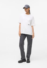 Hvid oversized t-shirt med trykt logo, parret med grå lige ben jeans og sorte platform støvler. En grå kasket fuldender outfittet.