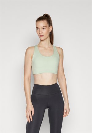 Soutien-gorge de sport vert clair avec un décolleté arrondi et des bretelles larges, fabriqué en tissu lisse et extensible. Associé à un legging noir taille haute.