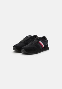 Scarpe da ginnastica nere realizzate con materiali in rete e suede, caratterizzate da un design a strisce bianche, rosse e blu sui lati e una suola nera testurizzata.
