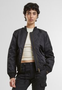 Schwarze Bomberjacke mit einem Frontreißverschluss, gerippten Bündchen und Kragen sowie zwei seitlichen Taschen. Glatte Textur mit minimalen Details.
