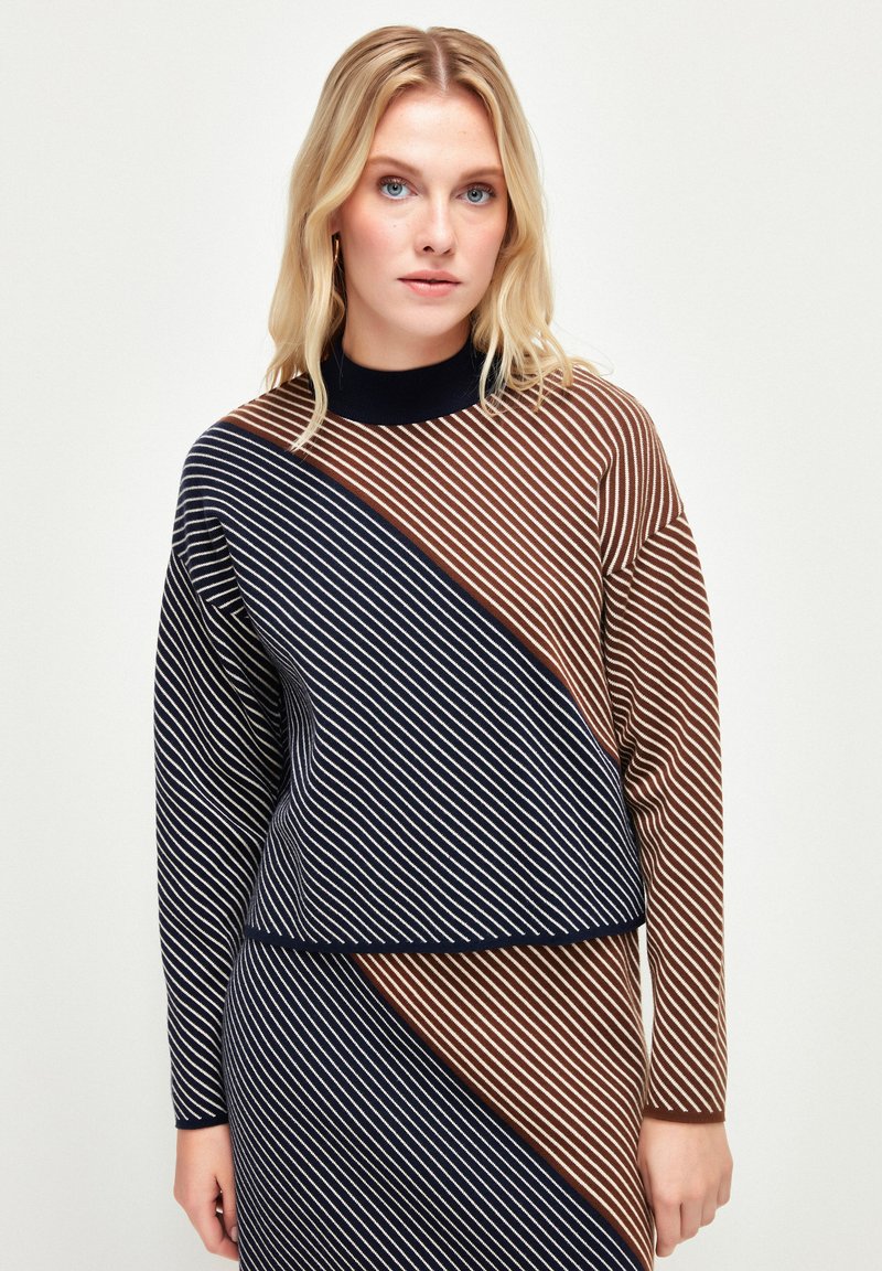 Sweter dzianinowy w diagonalne paski w kolorach granatowym, brązowym i kremowym, z wysokim dekoltem i luźnym krojem. Miękka tekstura, długie rękawy.