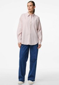 Heled roosa triibuline särk, millel on krae, pikad varrukad ja üks rinnatasku, koos lahtiste siniste teksade ja valgete tossudega.