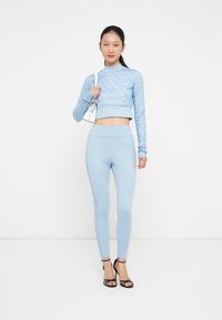 Világoskék aktív öltözet, amely egy texturált, rövidujjú, crop topból és egy magas derekú leggingsből áll, oldalt kontrasztos mintával.
