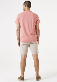 Camiseta de algodón rosa de manga corta para hombre combinada con pantalones cortos de rayas beige y zapatos marrones sin cordones, vista desde la parte de atrás.