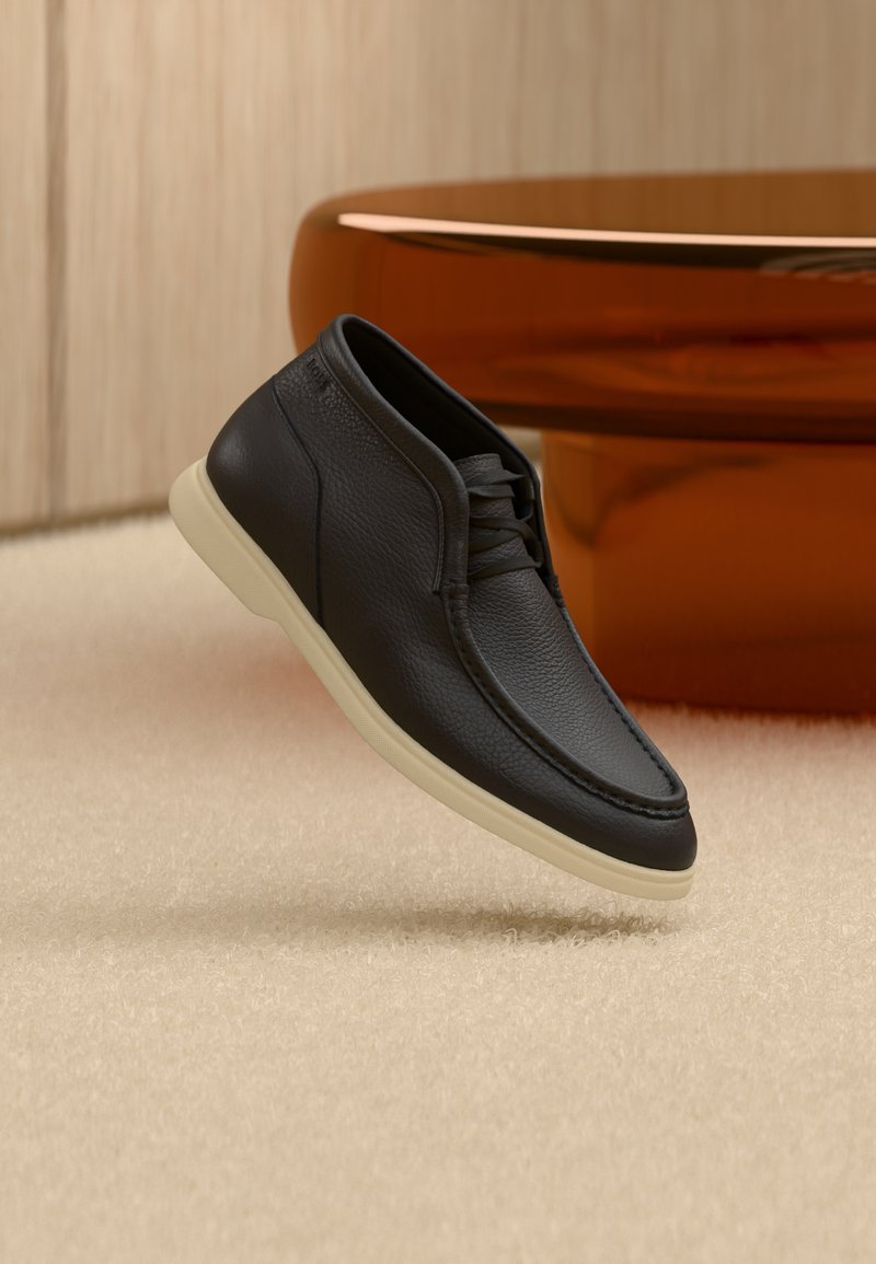 Chaussure en cuir noir avec une surface texturée, bout arrondi et semelle beige. Présente un design à lacets avec des coutures discrètes.