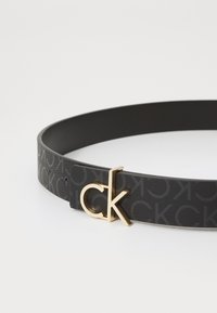 Čierny kožený opasok s textúrovaným povrchom, embosovaným logom a zlatým uzáverom v tvare "ck."