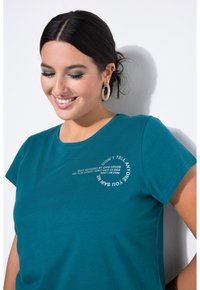 Teal katoenen T-shirt met korte mouwen en een ronde hals, voorzien van witte gebogen tekst op de voorkant. Zachte textuur, casual ontwerp.