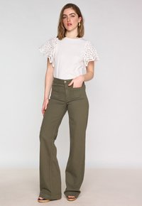 T-shirt blanc avec des manches en dentelle, associé à un pantalon taille haute en olive avec des jambes larges, et des sandales à plateforme beiges.