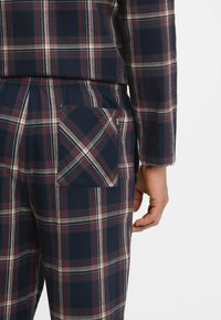 Marinblå rutig pyjamas av mjukt tyg med röda och vita detaljer, en knäppt ficka på baksidan och långa ärmar.