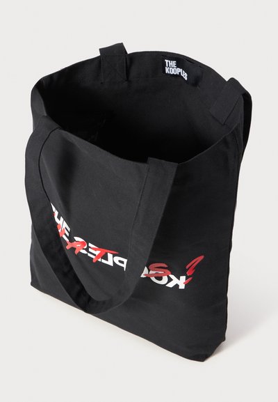 Black canvas tote bag with a wide opening, featuring printed red and white text on the front and sturdy fabric handles.