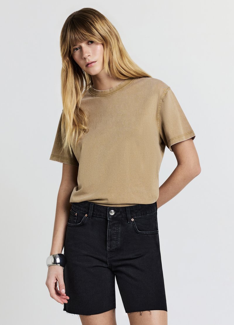 T-shirt en coton beige avec un col rond et des manches courtes, assorti à un short en denim foncé taille haute avec un ourlet brut et des accessoires en métal argenté.