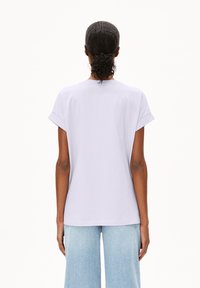 Lila kortemouw t-shirt met opgerolde manchetjes, ronde halslijn en een ontspannen pasvorm. Glad katoen, gedragen met lichtblauwe wijde jeans.