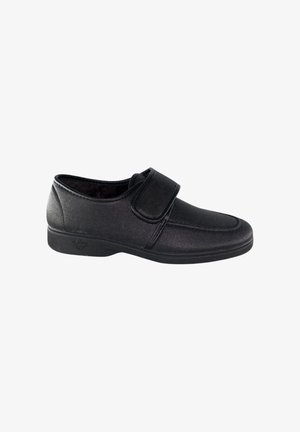 Zapato negro con tira de velcro, textura suave, punta redonda y suela de goma baja. Diseño minimalista adecuado para uso casual.