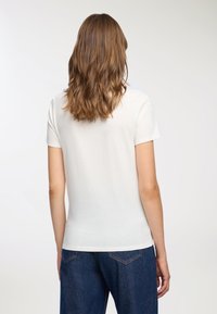 Biała koszulka z krótkim rękawem, dopasowana, wykonana z miękkiej bawełny, zestawiona z ciemnoniebieskimi dżinsami o wysokim stanie. Prosty, czysty design bez wzorów.