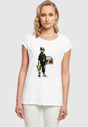 White cotton t-shirt featuring a graphic of a child in black with a yellow chain, holding a boombox and toy, set against a plain background.