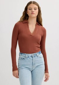 Top de manga larga de color óxido con cuello en V, combinado con jeans de tiro alto de color azul claro con una textura de mezclilla clásica.