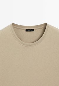 Beige T-Shirt mit rundem Ausschnitt, aus weicher Baumwolle gefertigt. Verfügt über ein sichtbares Markenlabel und eine glatte, gleichmäßige Textur.